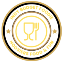 Indyfbudgetoodie.com logo is a circle with the words Indy Budget foodie and Hoosiers food & fun . In the center. there is a restaurant plate with a wine glass and fork.